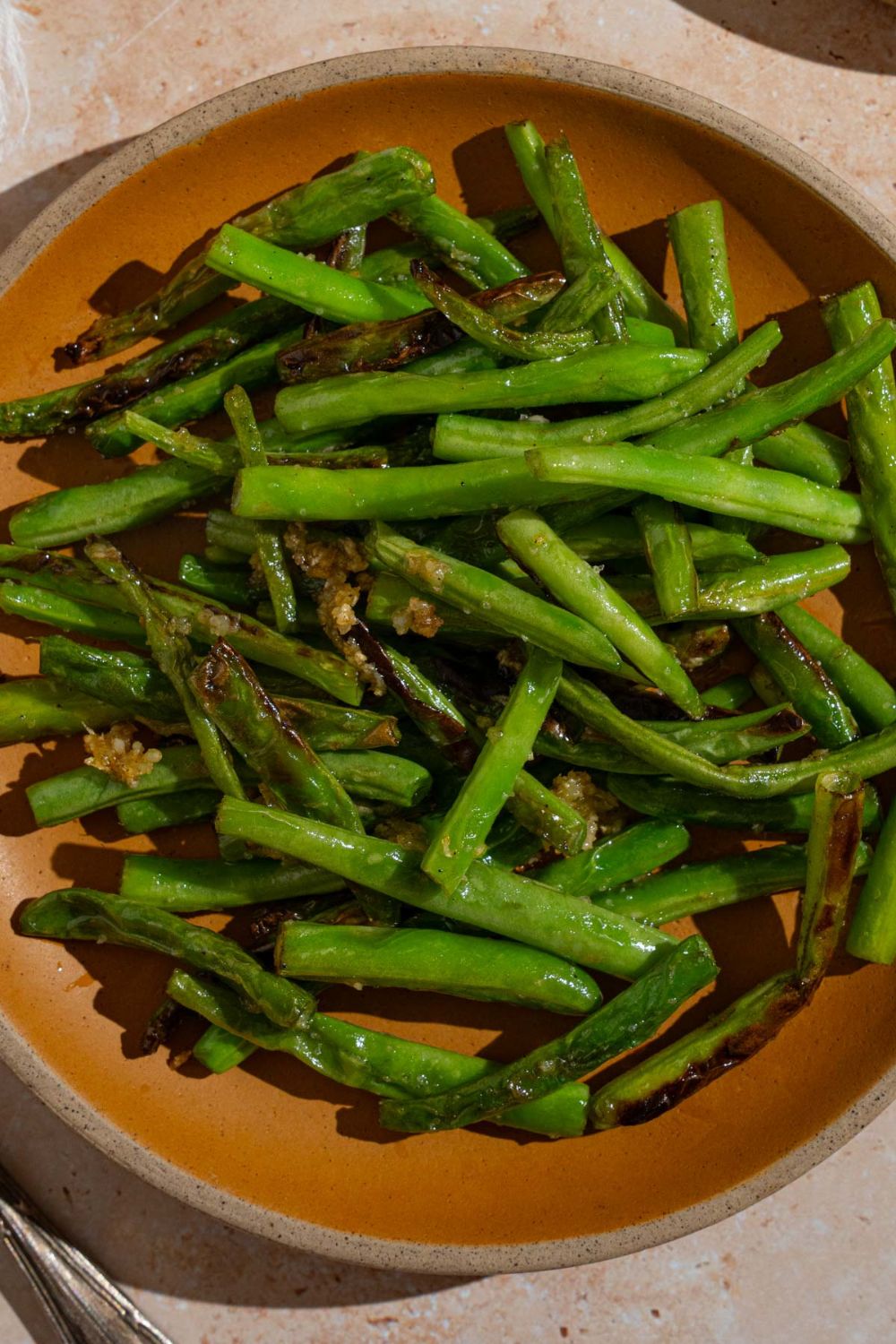 Copycat Din Tai Fung green beans tossed with roasted garlic on an orange plate. The plate is on a tan counter.