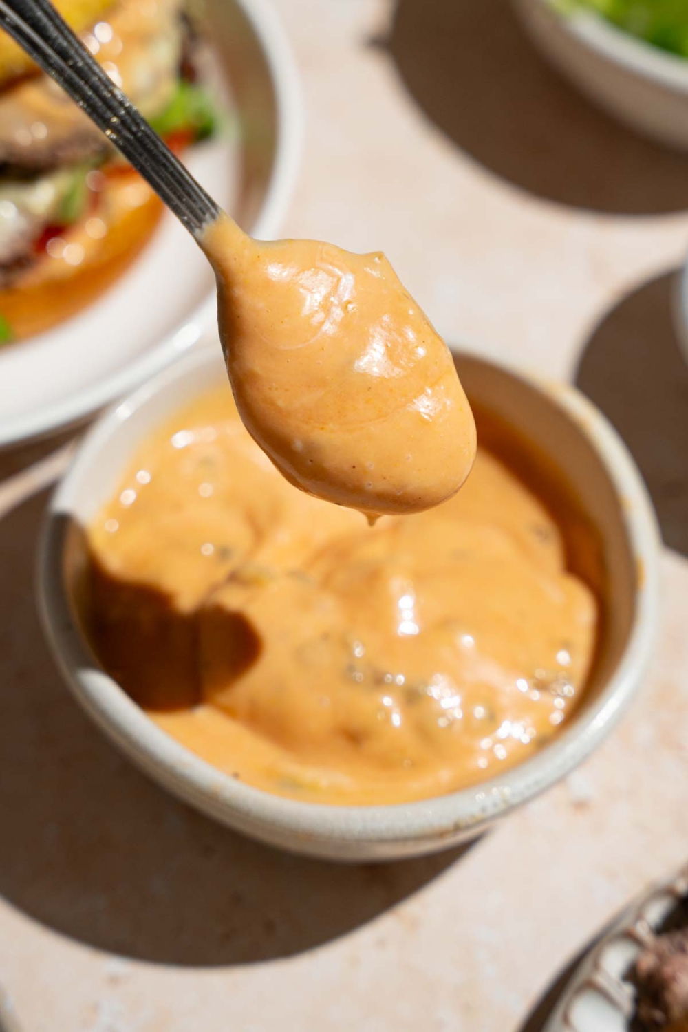 A close up of a spoon with In-n-Out sauce. There is a bowl of sauce on a tan counter blurred in the background.