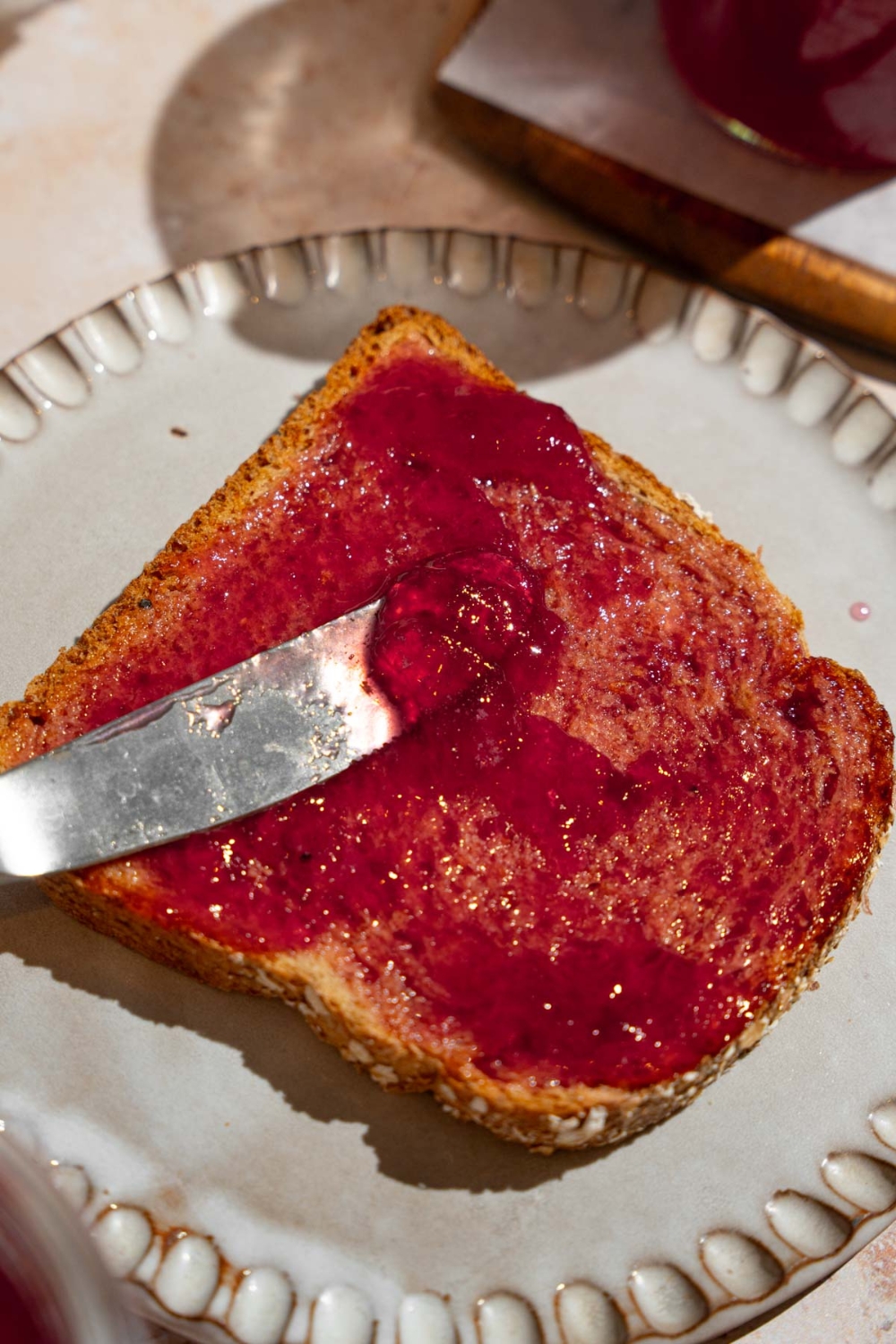 A knife spreading chokecherry jelly on a slice of toast. The toast is on a plate.