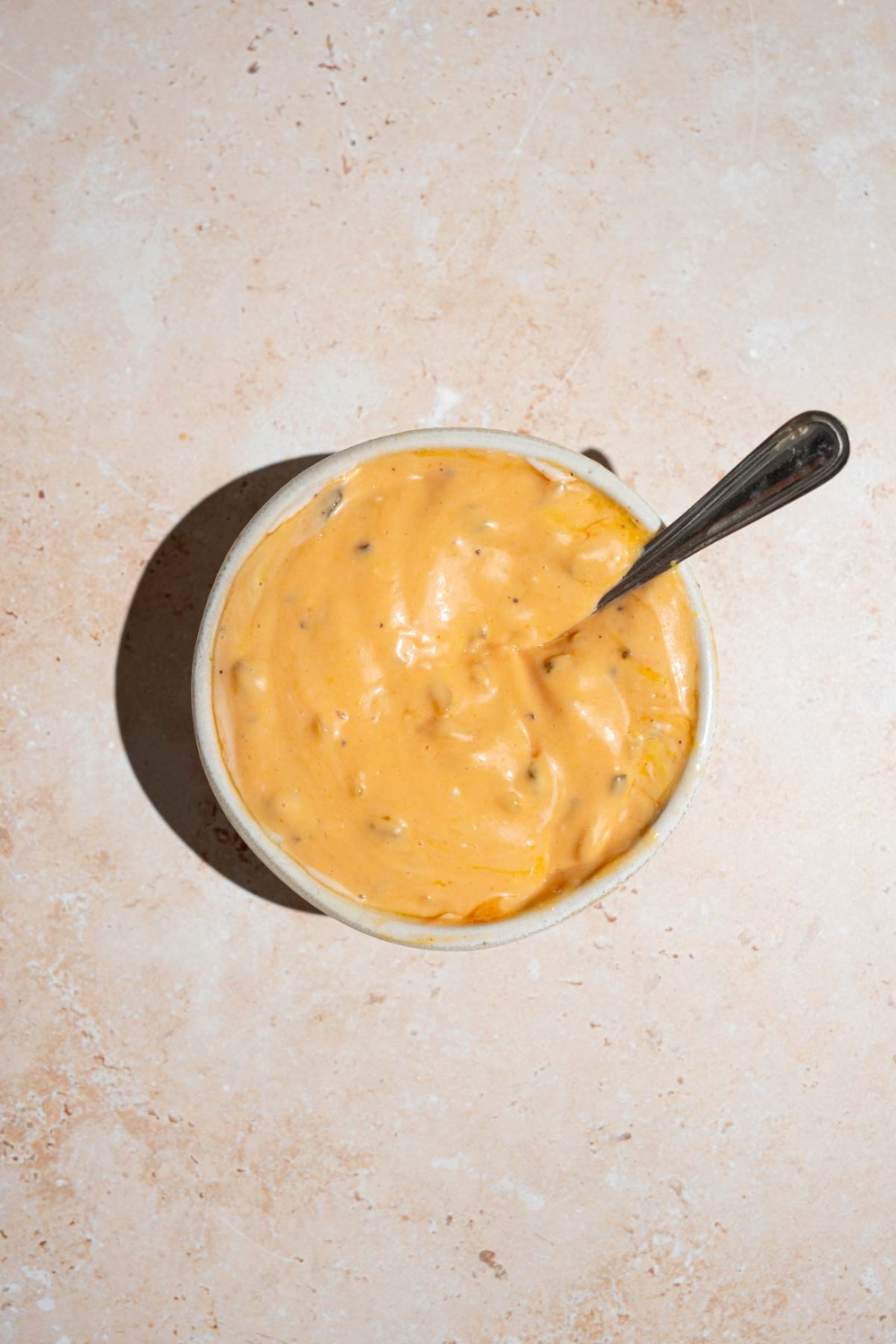 A white bowl with In-n-Out sauce with a spoon inside. The bowl is on a tan counter.