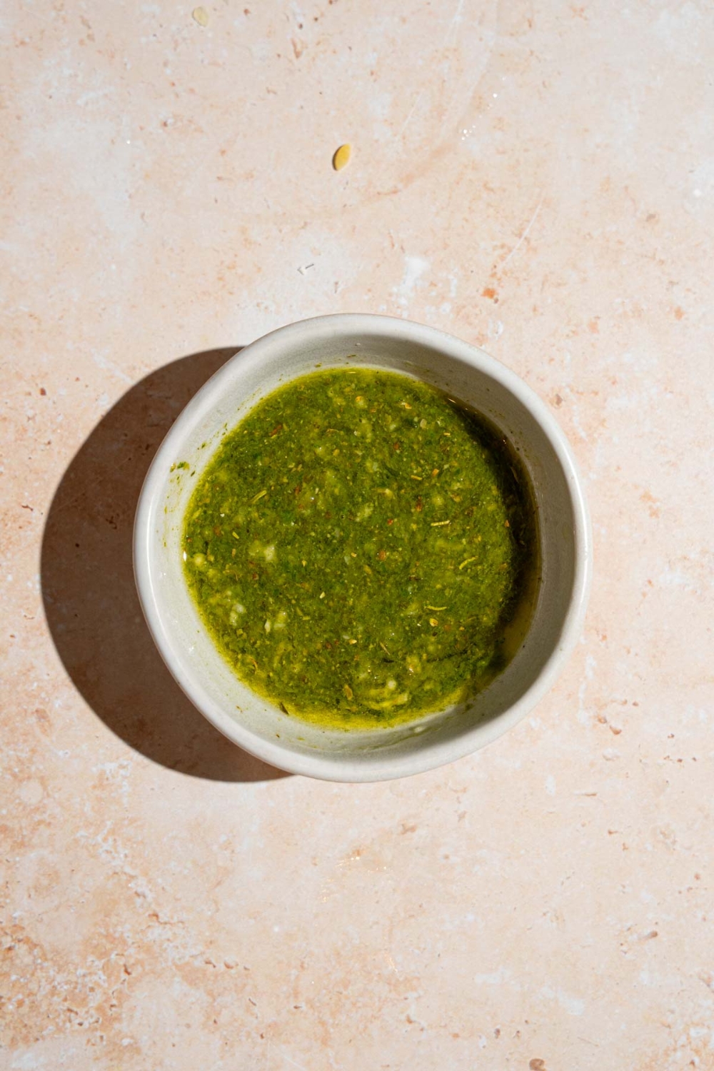 A small white bowl with Mediterranean pasta salad dressing. The bowl is on a tan counter.