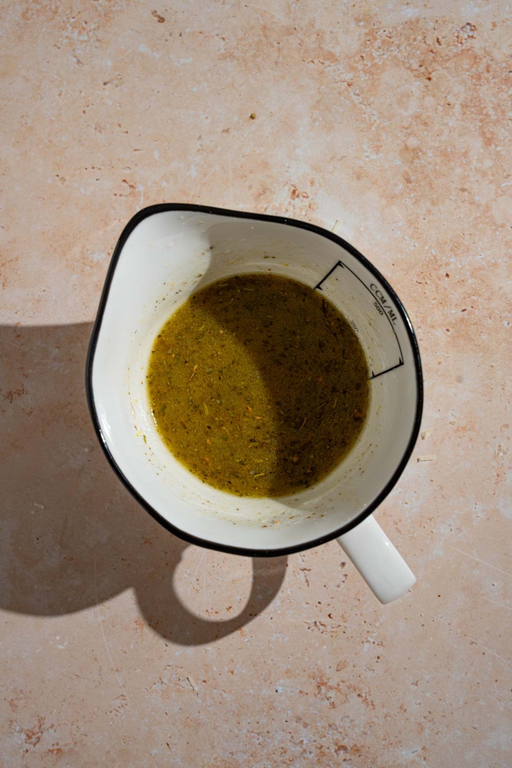 A bowl of combined copycat Texas Roadhouse italian dressing. The bowl is on a tan counter.