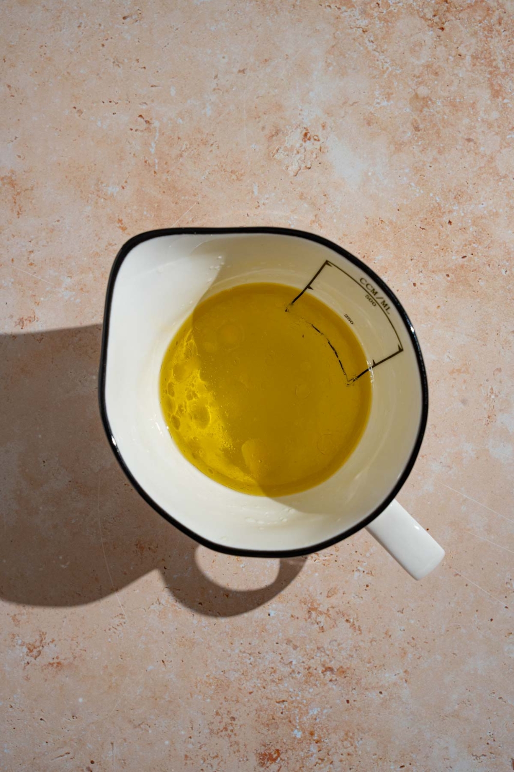 A bowl with olive oil and vinegar. The bowl is on a tan counter.