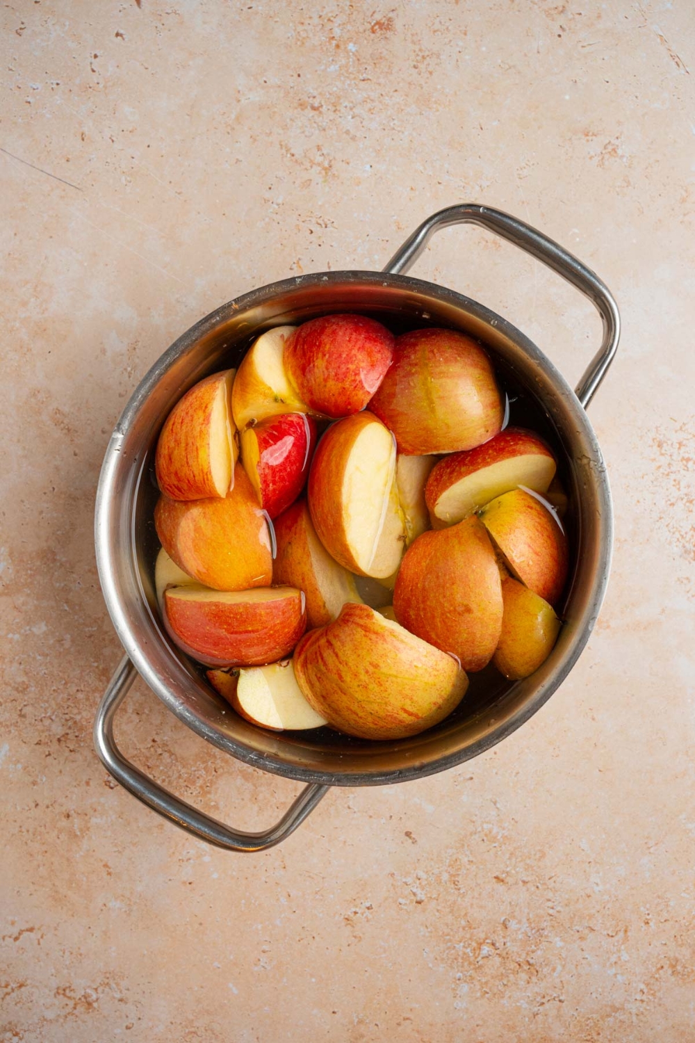 A stock pot of halved apples in water. The pot is on a tan counter.