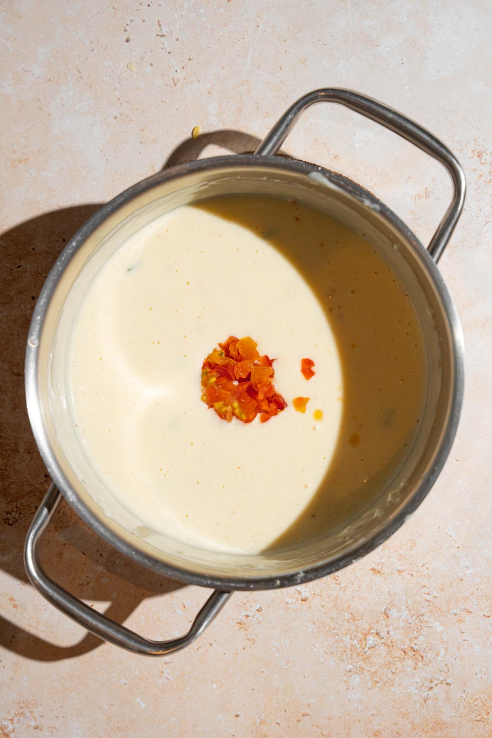 A stock pot with cooked Chipotle queso topped with chopped tomatoes. The pot is on a tan counter.
