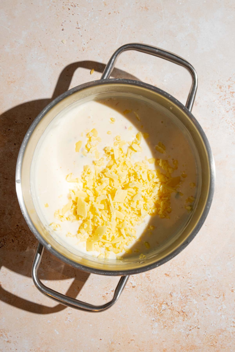 A stock pot with Chipotle queso topped with shredded white cheddar. The pot is on a tan counter.
