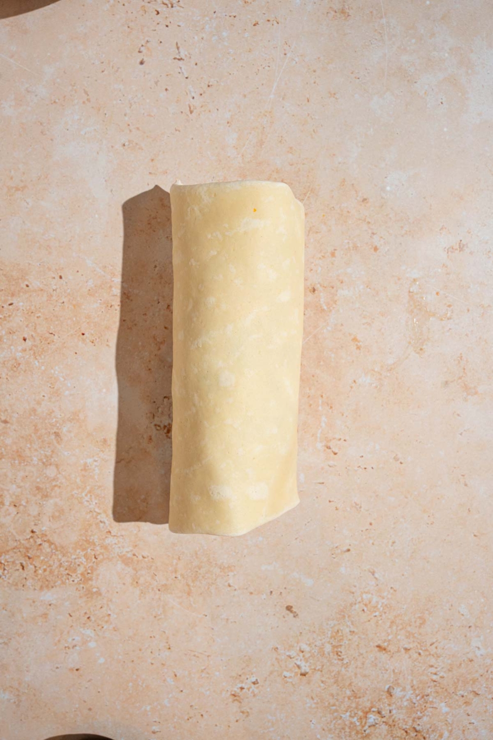 An uncooked cheesy garlic chicken wrap. The wrap is on a tan counter.