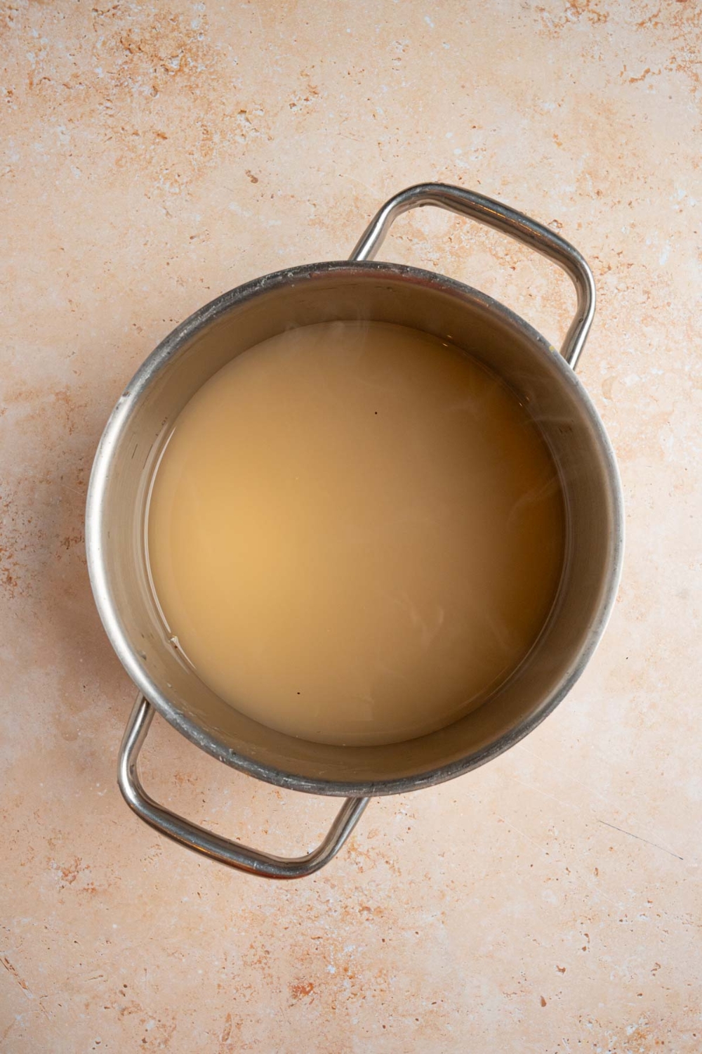 A stock pot with simmered apple juice, sugar, and lemon juice. The pot is on a tan counter.