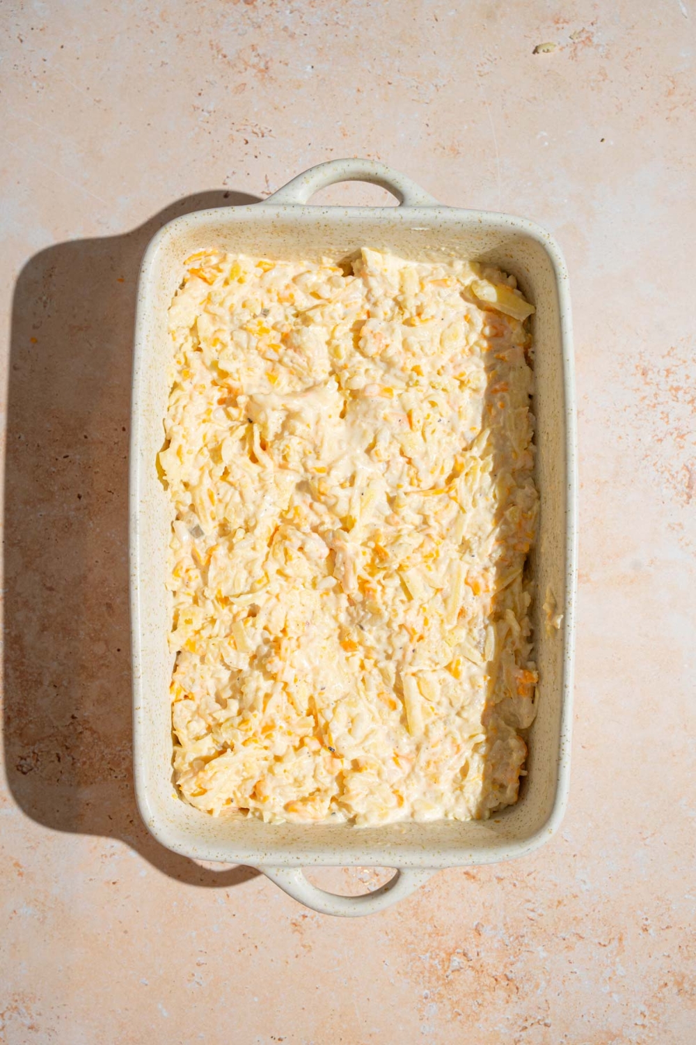 A baking dish with uncooked party potatoes casserole on a tan counter.