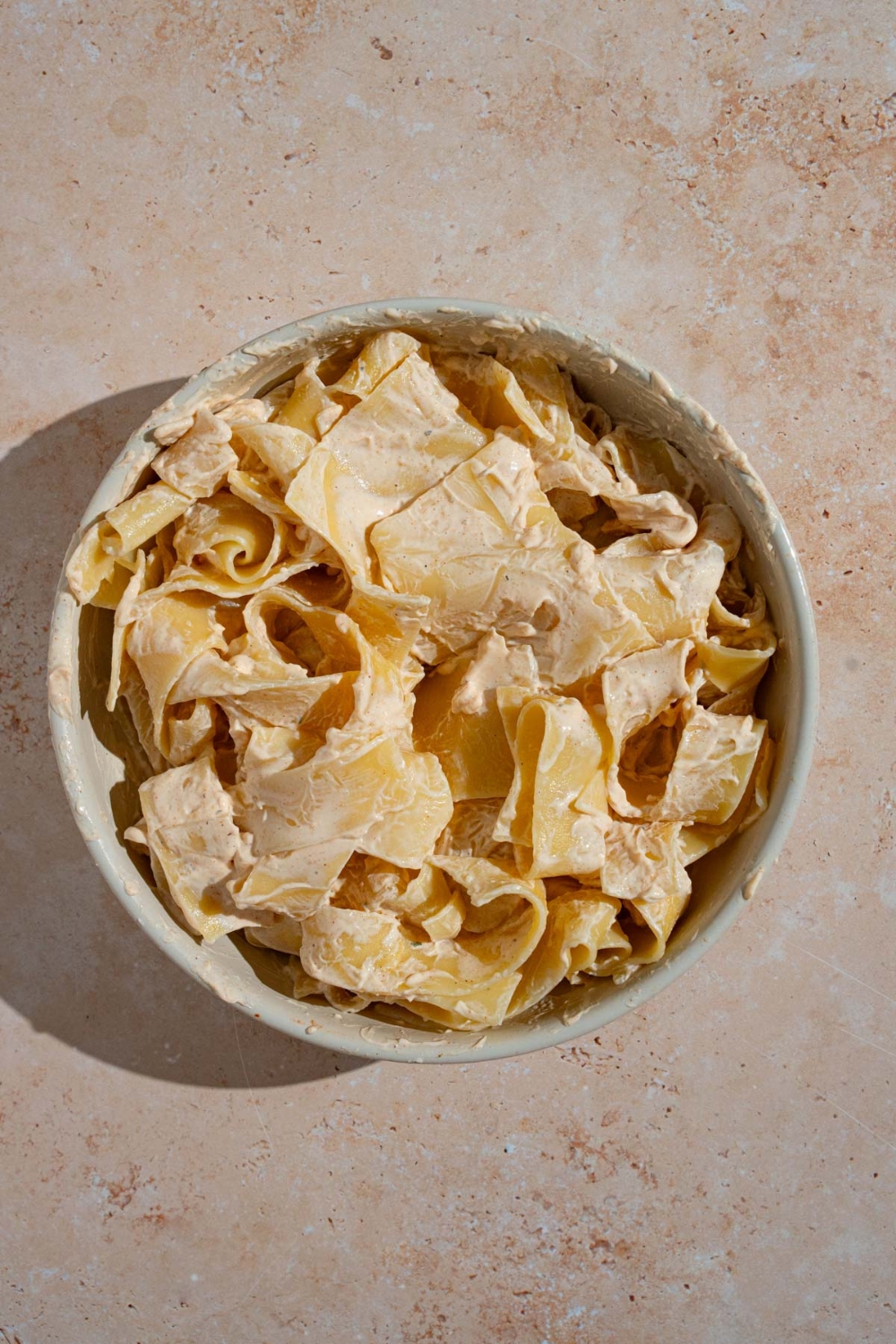 A bowl of wide egg noodles coated in a cream cheese mixture. The bowl is on a tan counter.