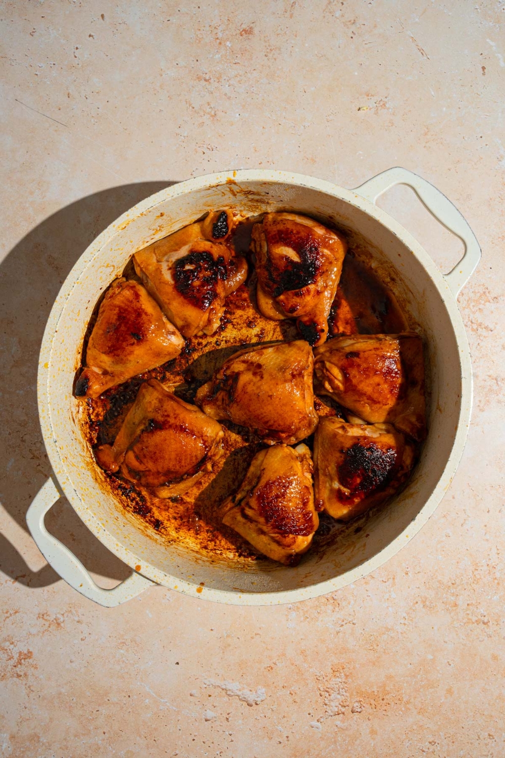 A large ceramic pot with seared marinated chicken thighs. The pot is on a tan counter.