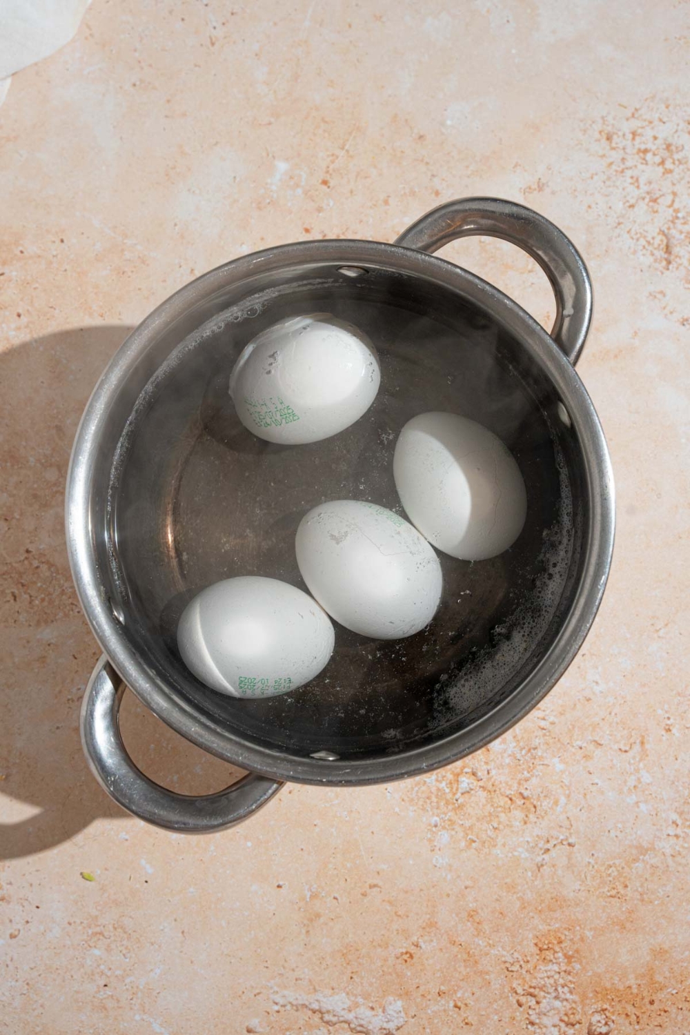 A stock pot with four eggs cooking in water. The pot is on a tan counter.