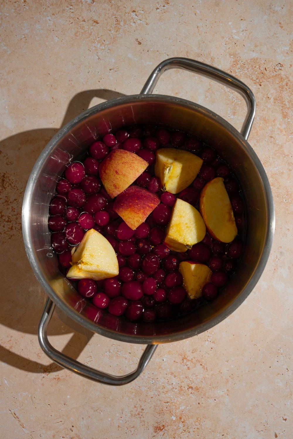 A stock pot with whole chokecherries and quartered apples. The pot is on a tan counter.