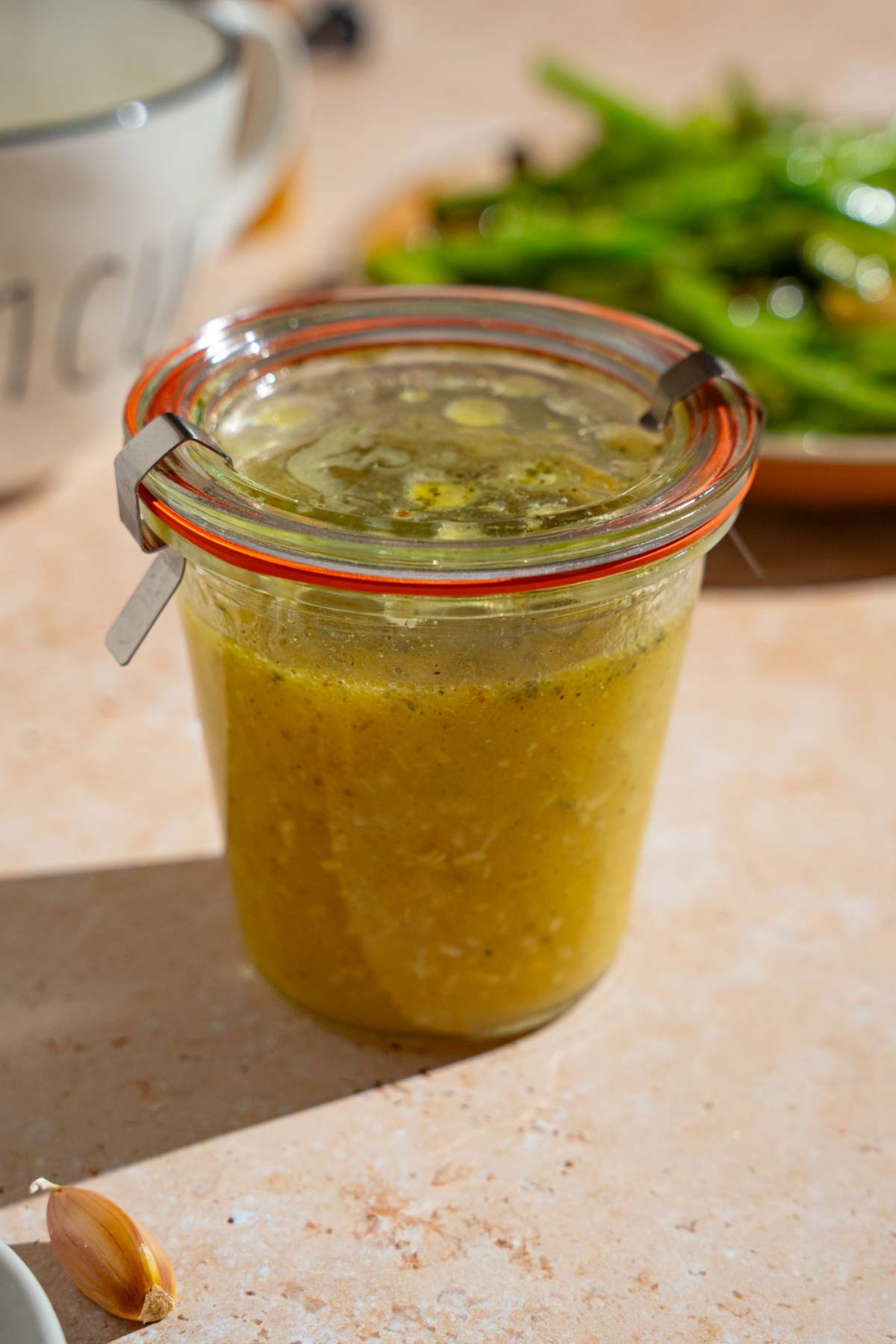 A sealed jar of copycat Texas Roadhouse italian dressing. The dressing is on a tan counter with a plate of green beans.
