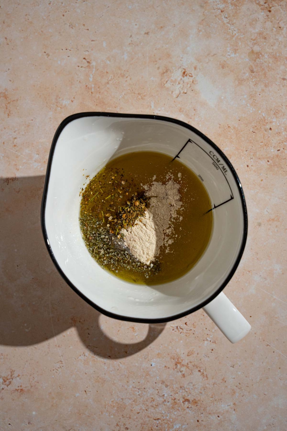 A bowl with an olive oil mixture with seasonings on top. The bowl is on a tan counter.