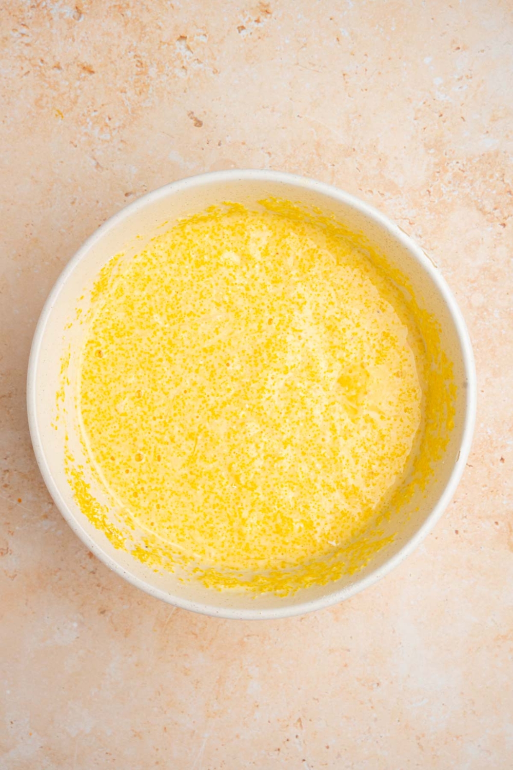 A large white bowl with a cornbread batter mixture. The bowl is on a tan counter.