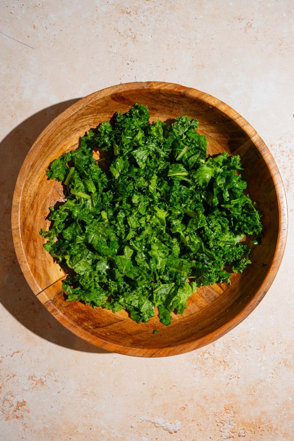 A salad bowl with chopped kale. The bowl is on a tan counter.