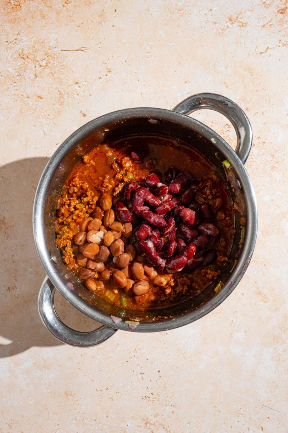 A stock pot with copycat Zippy's chili mixture including kidney beans, pinto beans, tomato sauce, and cooked beef. The pot is on a tan counter.