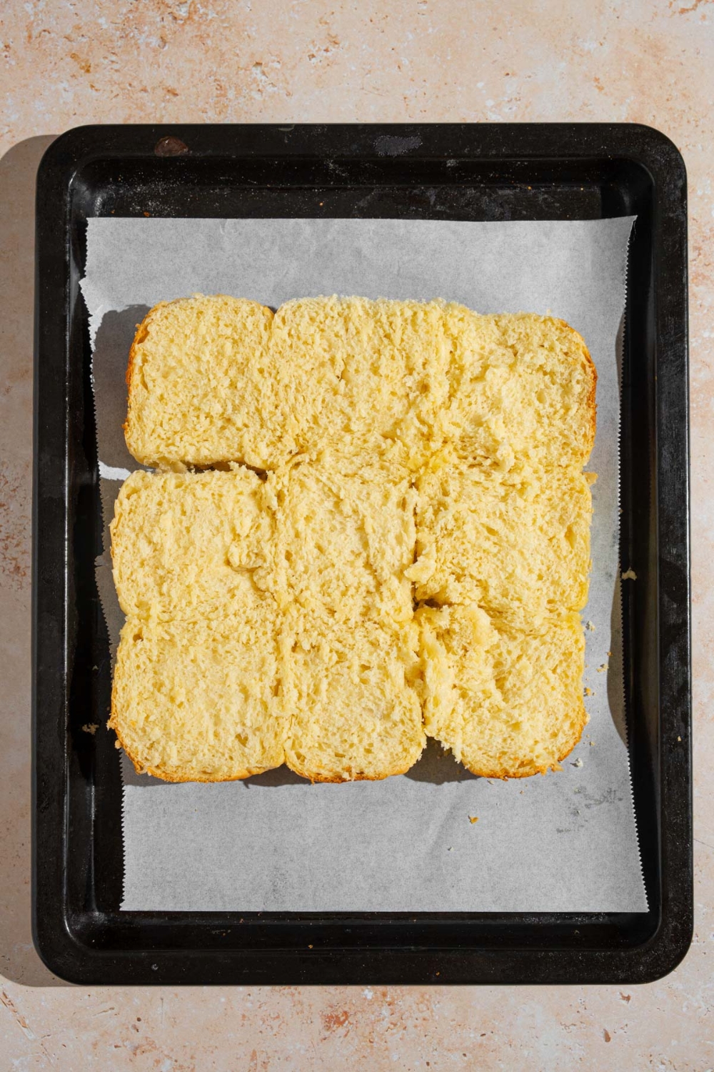 A baking sheet lined with parchment paper with nine open slider rolls.