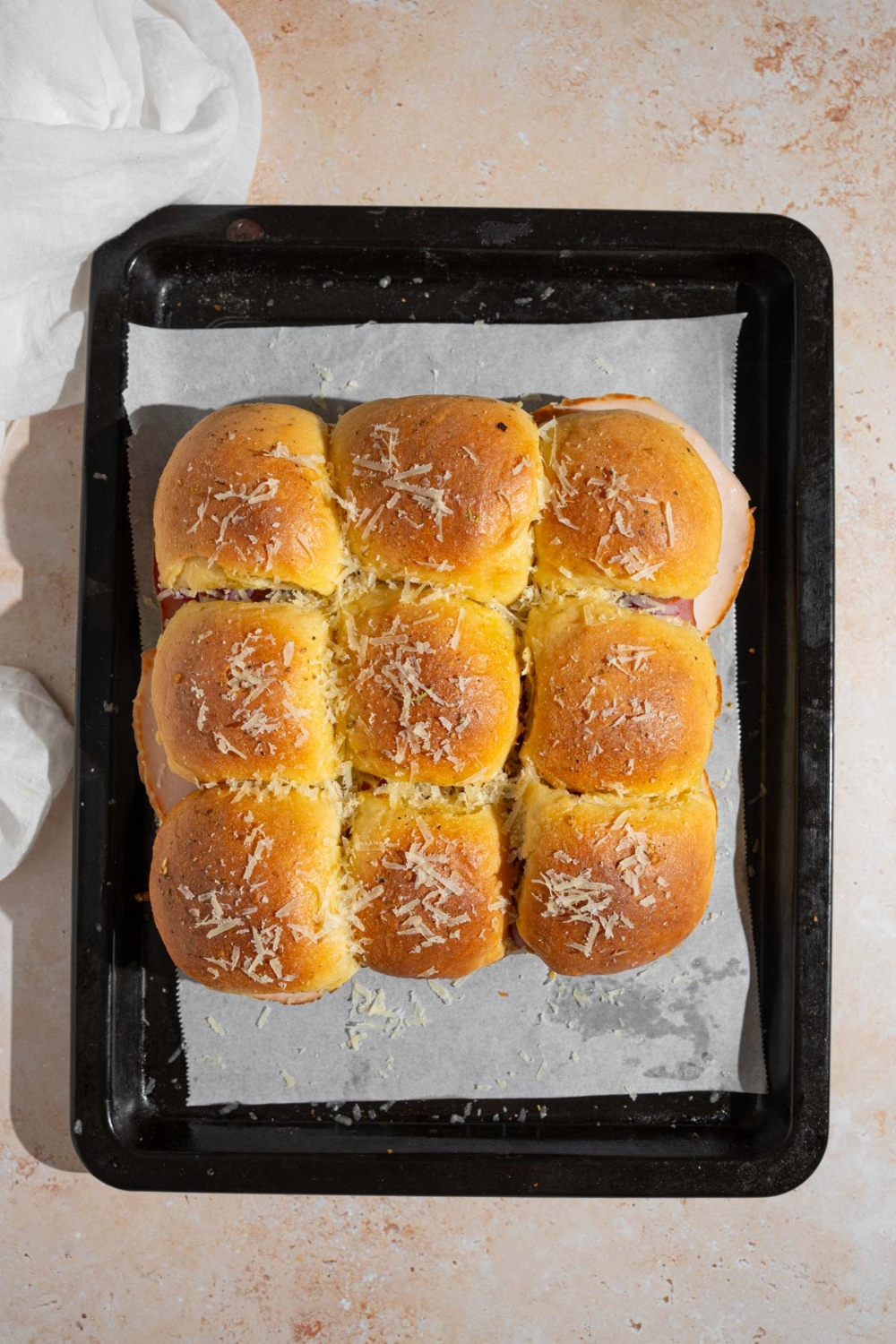 A baking sheet lined with parchment paper with nine Italian sliders topped with grated cheese and seasonings.