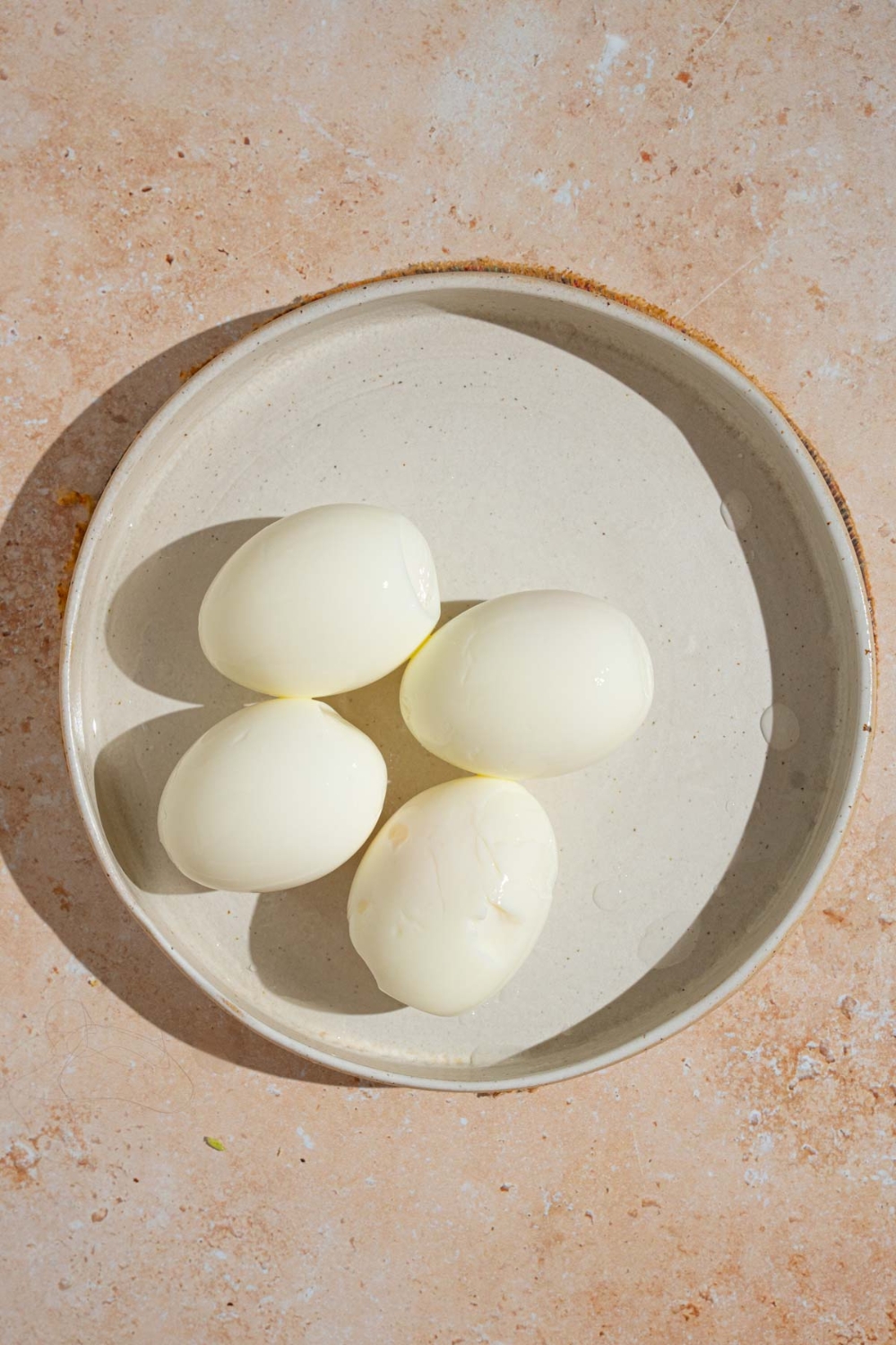 A plate with four hard boiled eggs. The plate is on a tan counter.