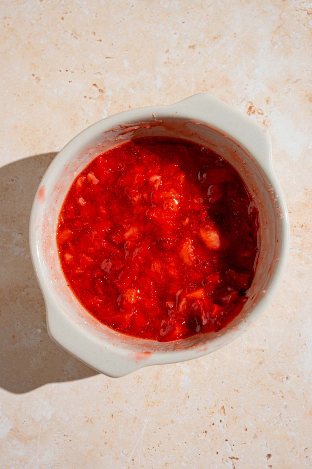 A small bowl with macerated strawberries. The bowl is on a tan counter.