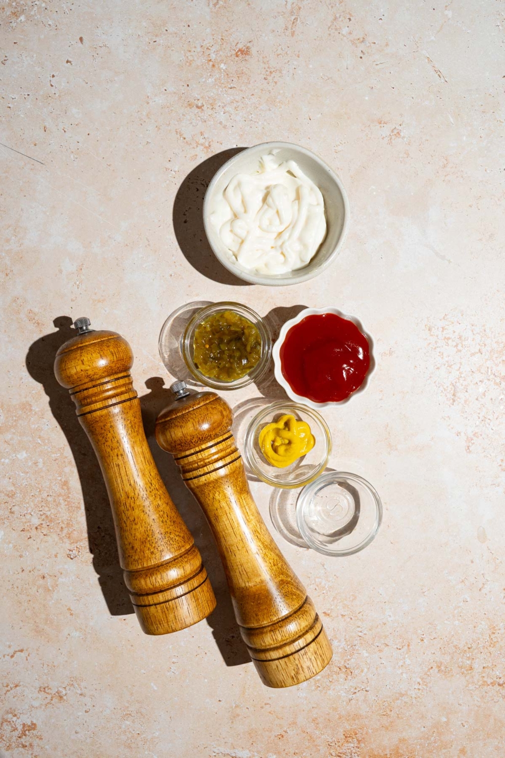 An overhead shot of several bowls in various sizes containing ingredients to make copycat In-N-Out sauce including ketchup, mayo, mustard, relish, vinegar, and a salt and pepper mill.