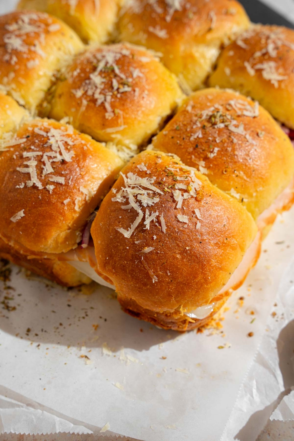 A tray of Italian sliders topped with grated cheese and seasonings.