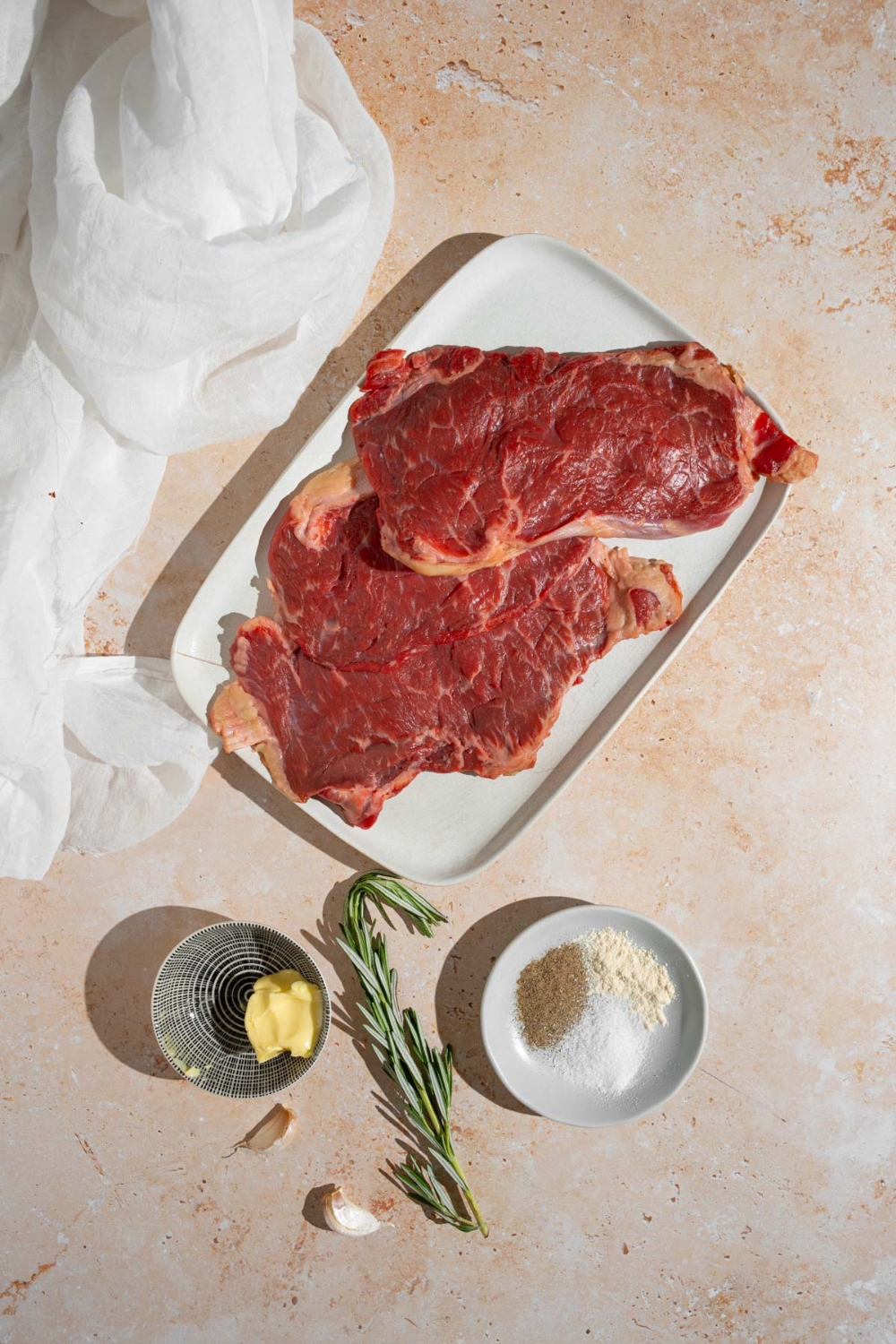 An overhead shot of several ingredients to make one-minute steaks including sirloin steaks, butter, a sprig of rosemary, and seasonings.