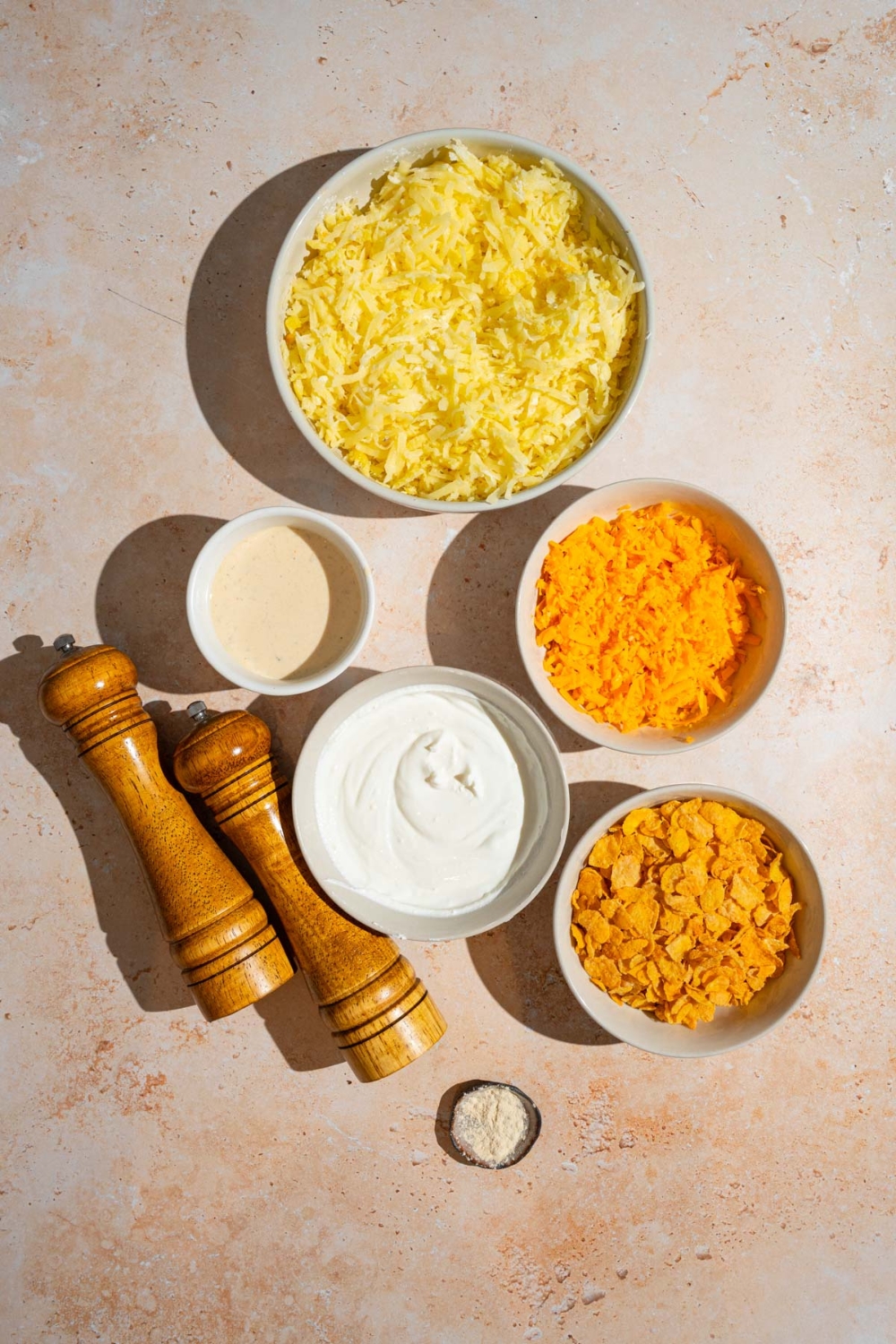An overhead shot of several bowl in various sizes containing ingredients to make party potatoes including shredded hashbrowns, sour cream, cream of chicken soup, corn flakes, cheddar cheese, and seasonings.