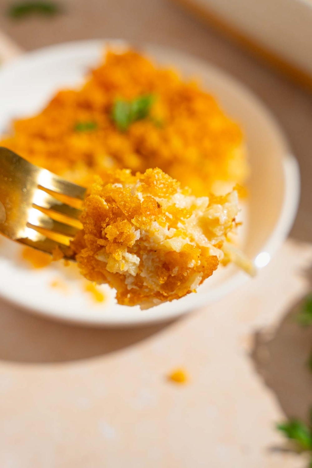 A close up of a fork with a bite of party potatoes with a plate of potatoes blurred in the background.