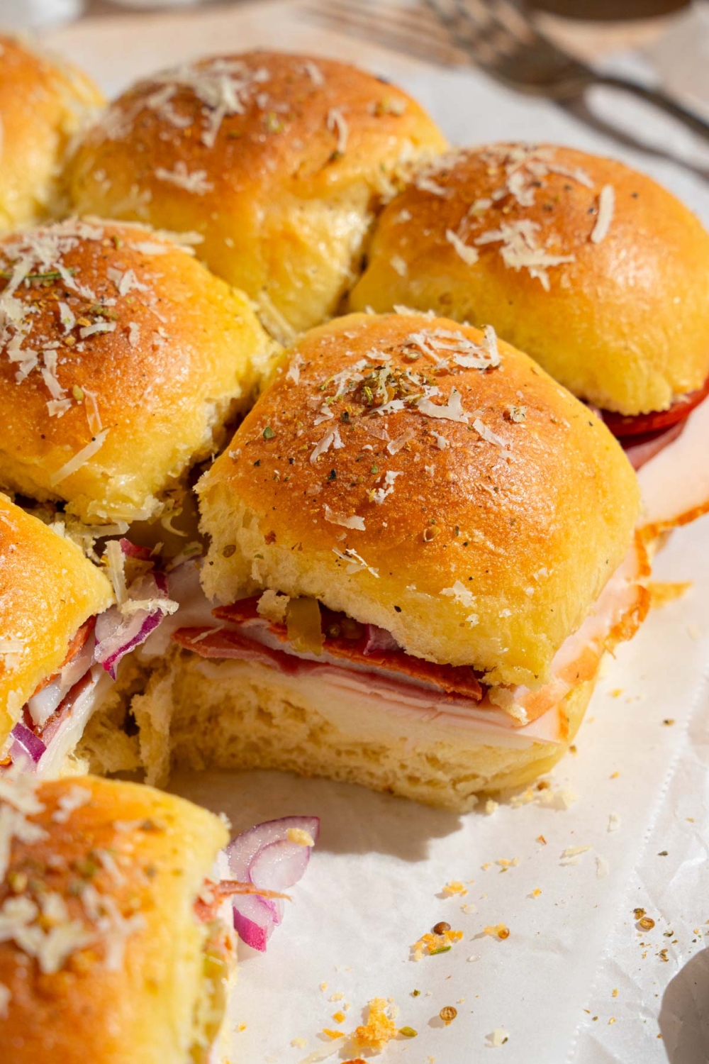 An array of Italian sliders topped with grated cheese and seasonings. The sliders are on sheets of parchment paper.