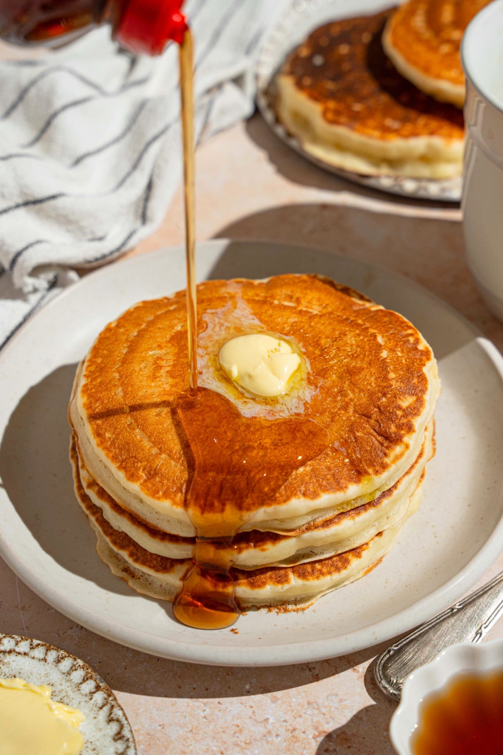 Maple syrup being poured on top of three pancakes on a white plate.