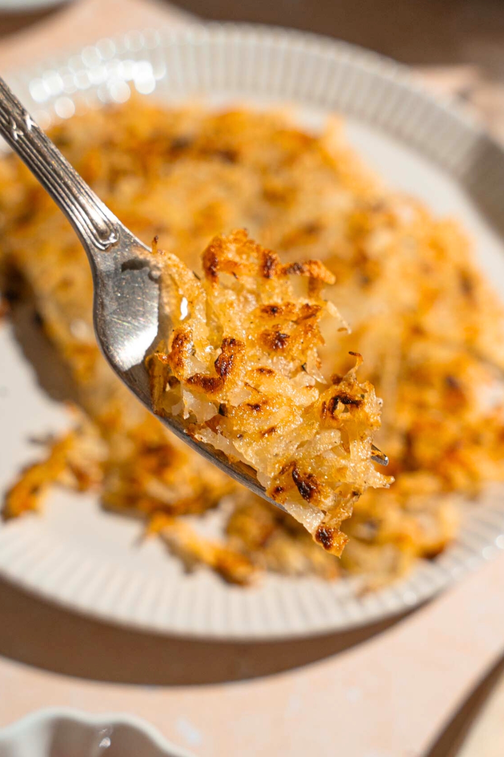 Hash browns on a fork hovering over a white plate with hash browns on it.