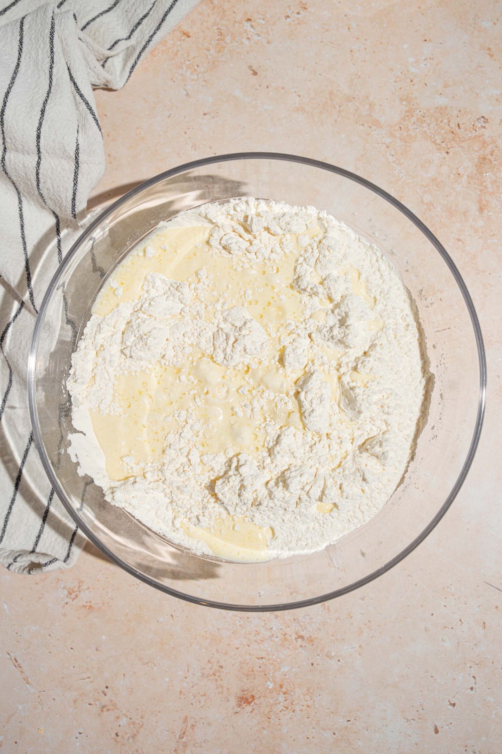 A bowl of flour with some milk in it in a glass bowl.