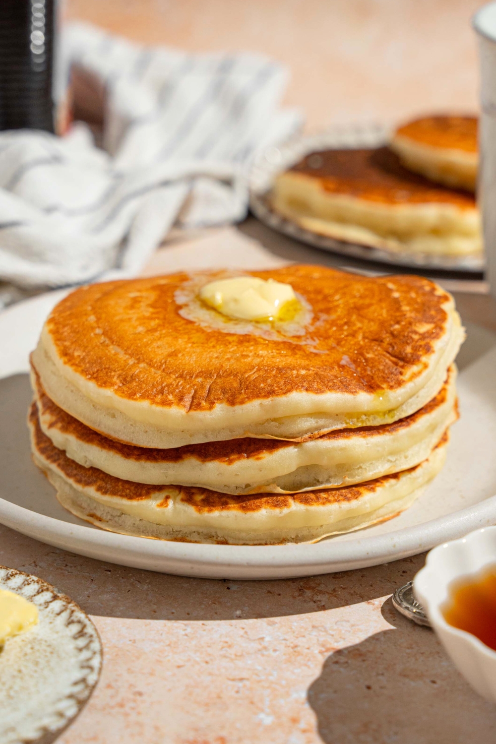 Three pancakes with a slab of butter on them on a white plate.