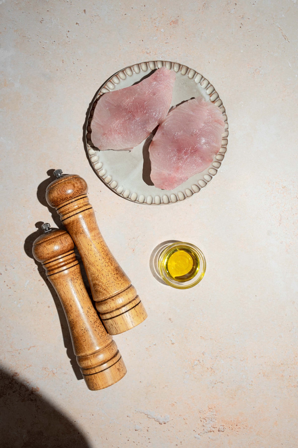 An overhead shot of ingredients to make pan seared swordfish including two swordfish fillets, oil, and salt and pepper mills