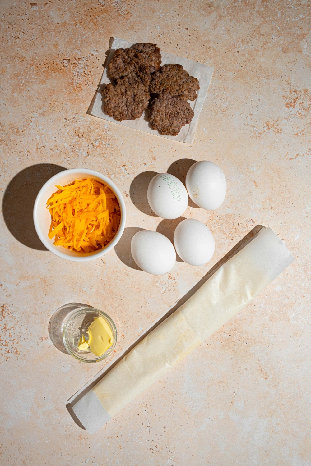 An overhead shot of several ingredients to make breakfast hand pies including eggs, shredded cheddar cheese, breakfast sausage patties, butter, and puff pastry