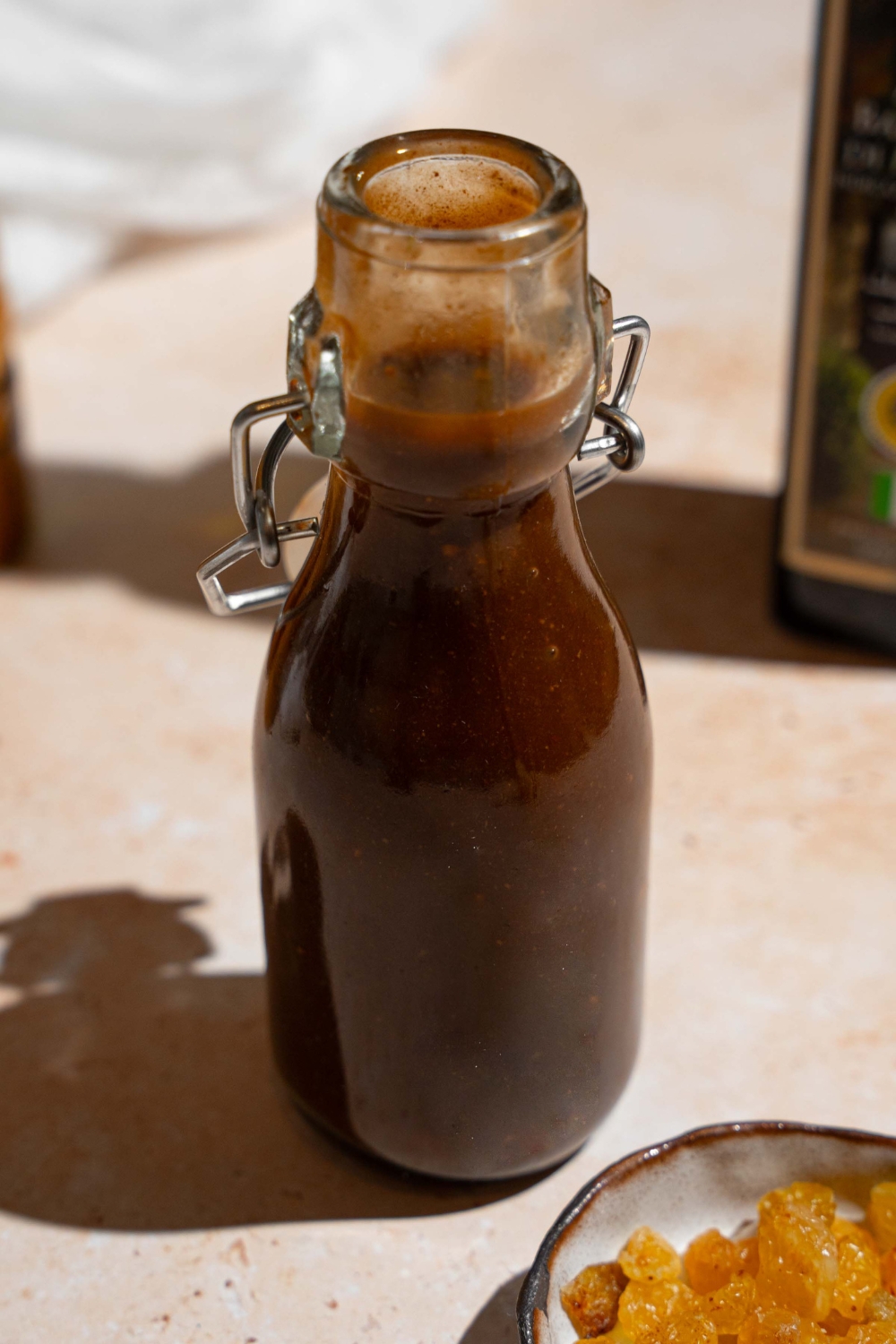 An open condiment jar of homemade A1 steak sauce. The jar is on a tan counter with a small plate of raisins and a white cloth napkin.