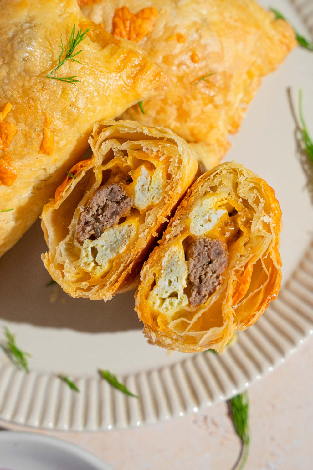 A five ingredient breakfast hand pie sliced in half on a white plate garnished with fresh herbs.