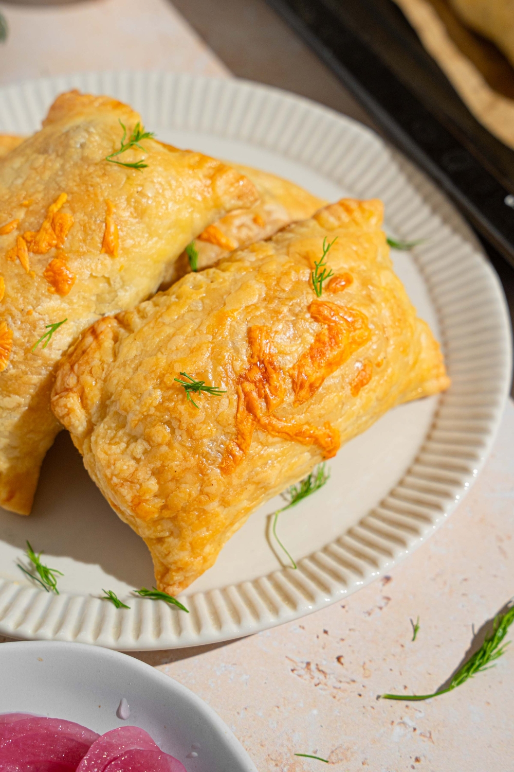 Several five ingredients breakfast hand pies on a white plate garnished with fresh herbs. The plate is on a tan counter.