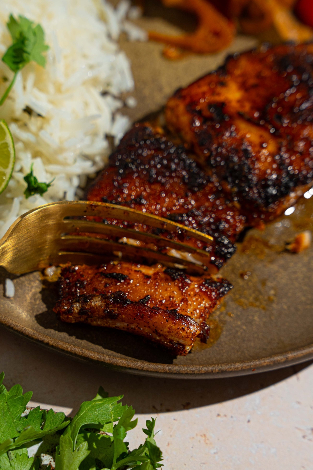 Blackened grouper on a gray ceramic plate with rice garnished with fresh parsley. There is a fork taking a bite of salmon.