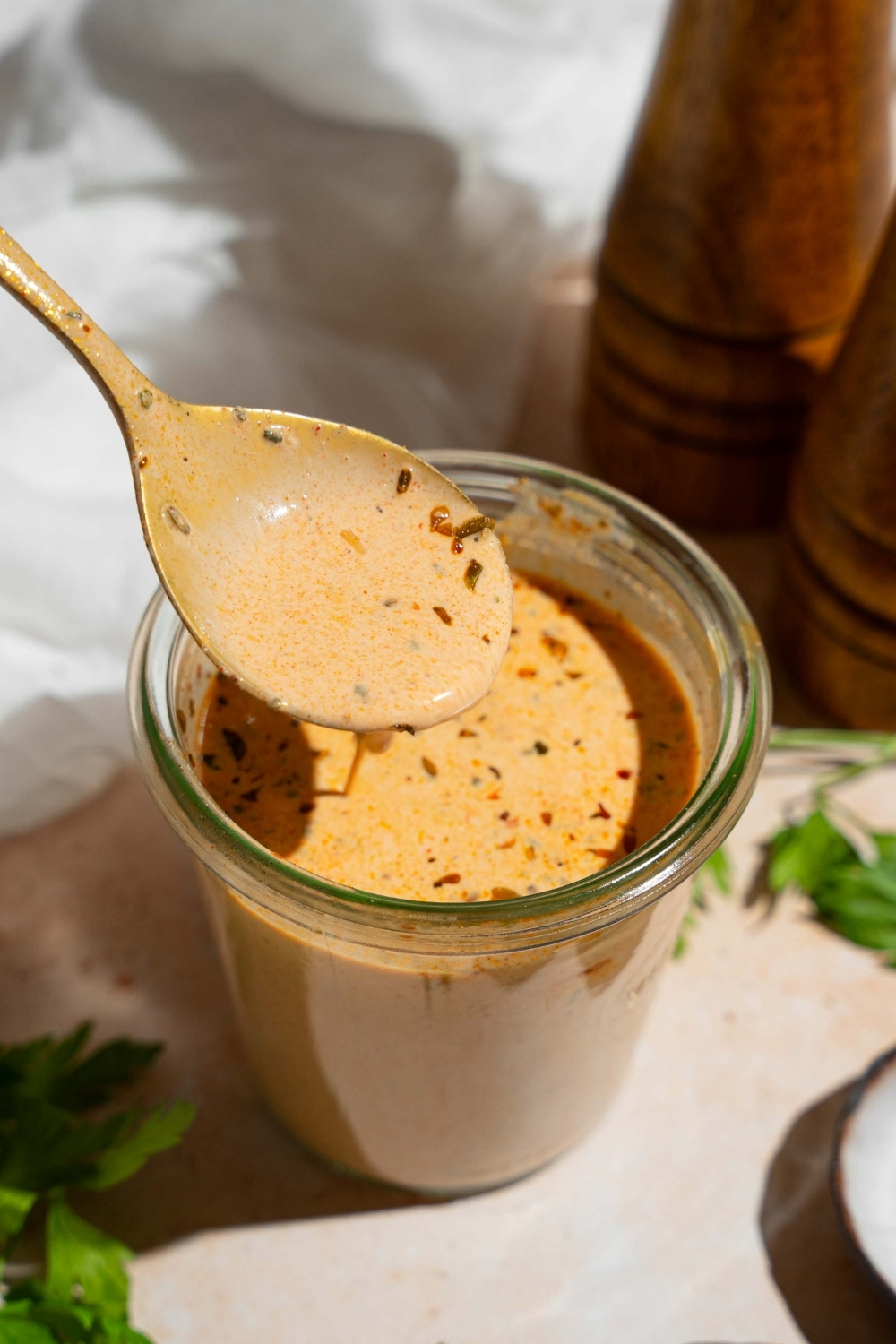 A glass jar of cajun cream sauce with a spoon dipping into the sauce. The jar is on a tan counter with a white cloth napkin and salt and pepper mill.