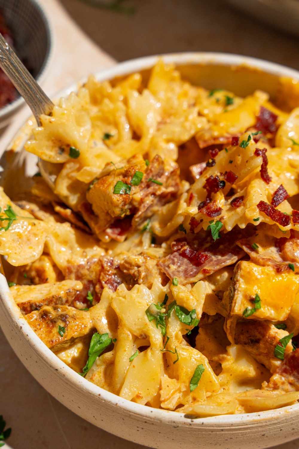 A white bowl with chicken bacon ranch pasta garnished with fresh parsley. There is a fork in the bowl.