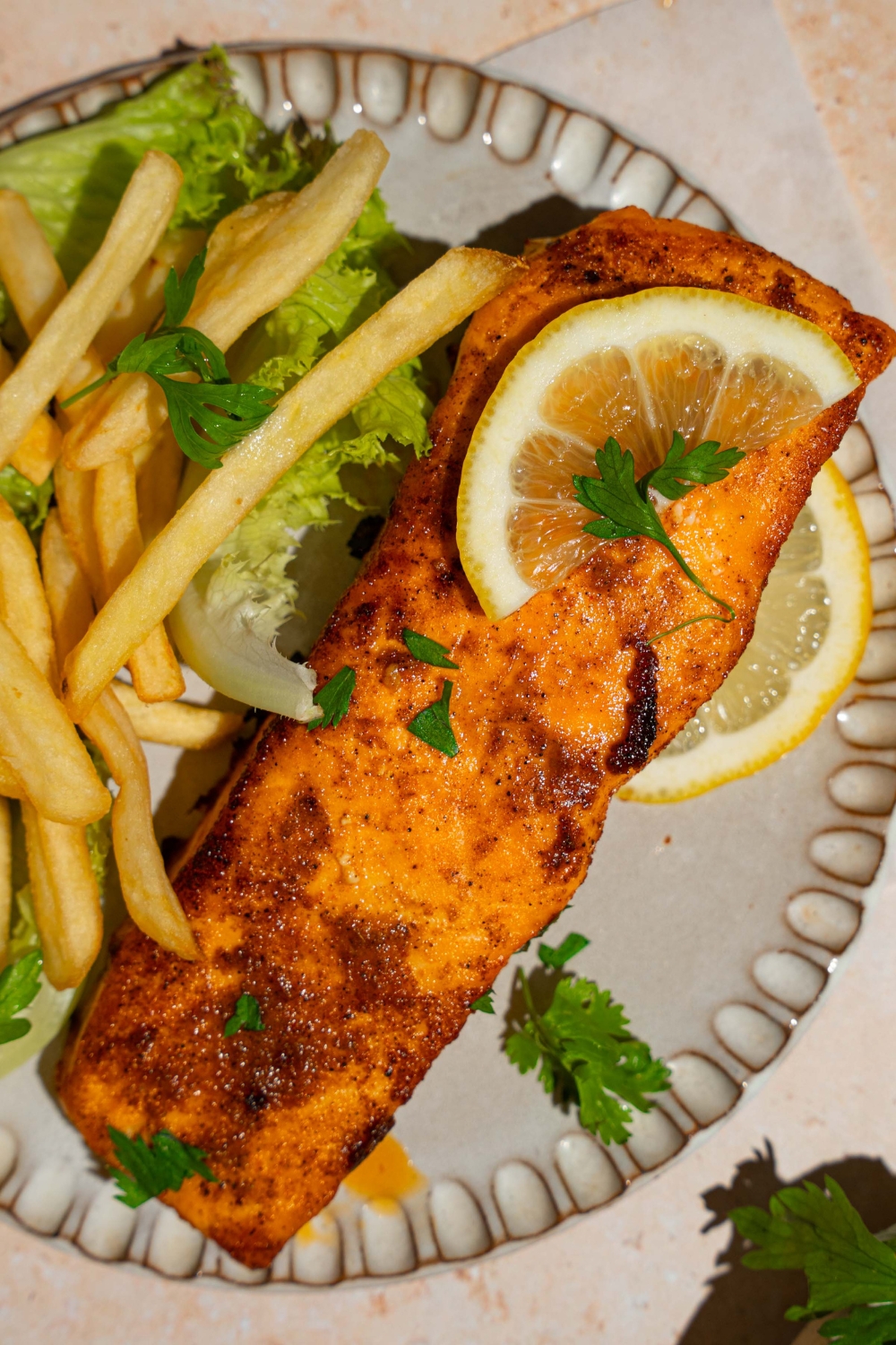 A ceramic plate with frozen air fryer salmon served with lettuce and french fries and garnished with fresh parsley and lemon.