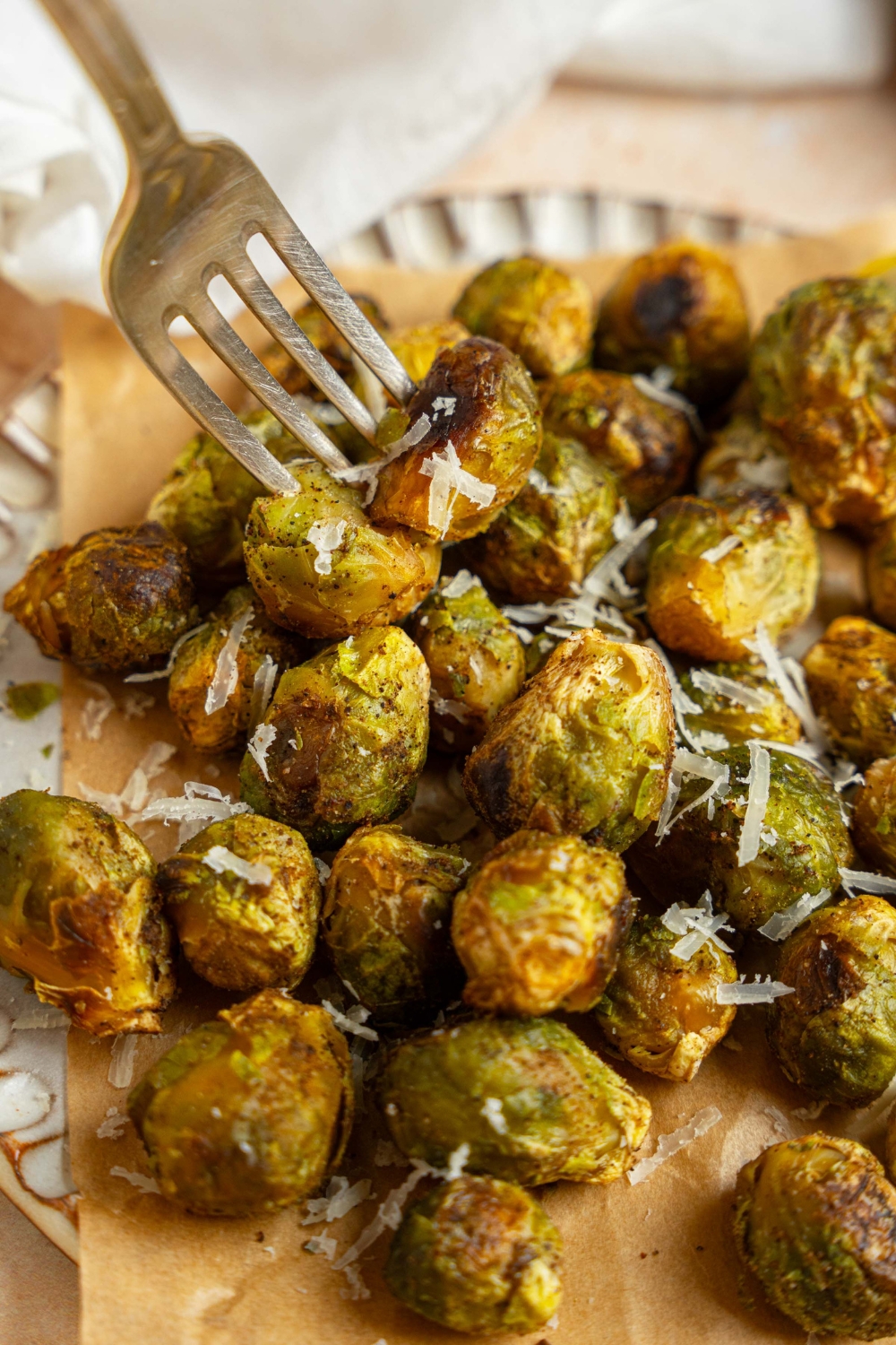 A ceramic plate lined with parchment paper garnished with grated parmesan. There is a fork taking a bite of brussel sprouts.
