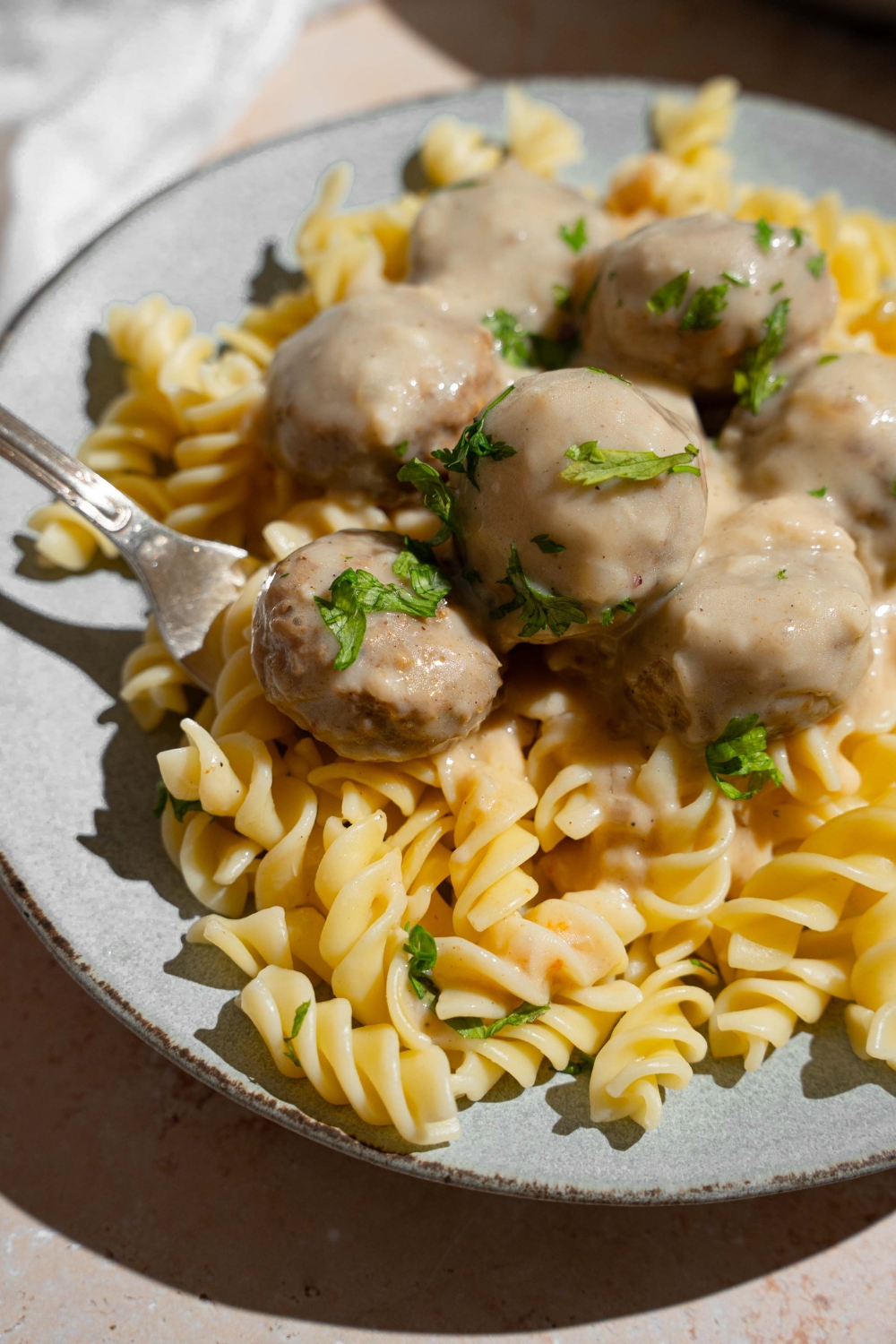 A ceramic plate with pasta topped with Swedish meatballs garnished with fresh parsley. There is a fork in the pasta.