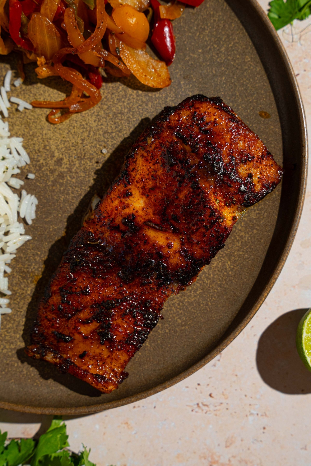 Blackened grouper on a gray ceramic plate with rice garnished with fresh parsley.