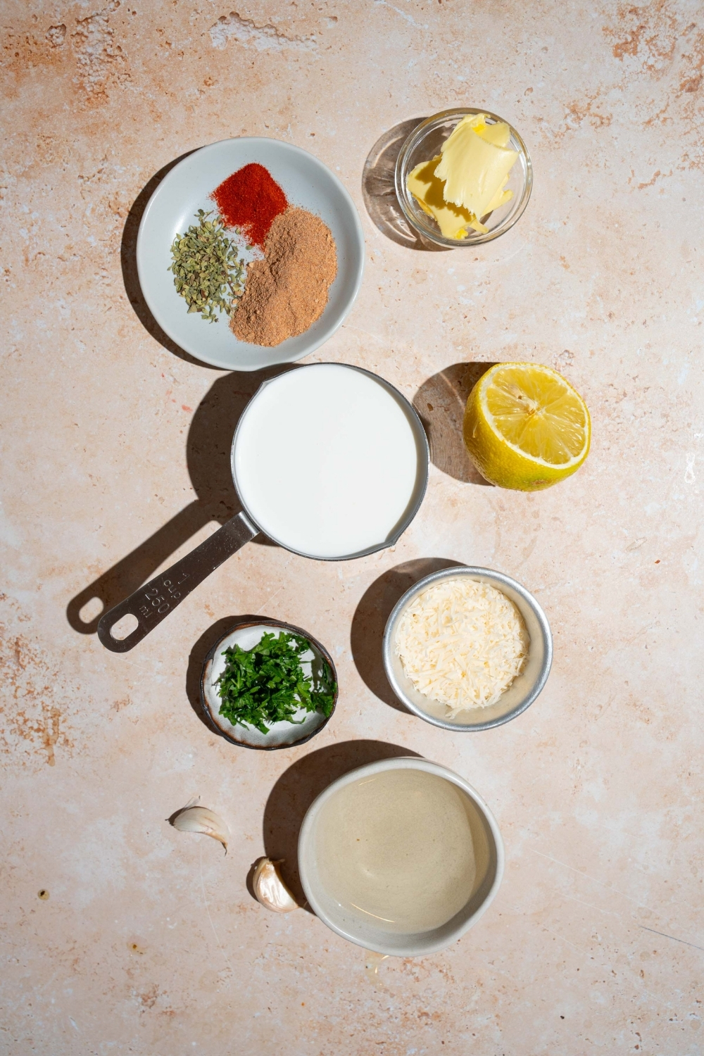 An overhead shot of several bowls in various sizes containing ingredients to make cajun cream sauce including cream, white wine, lemon, butter, garlic, and seasonings.