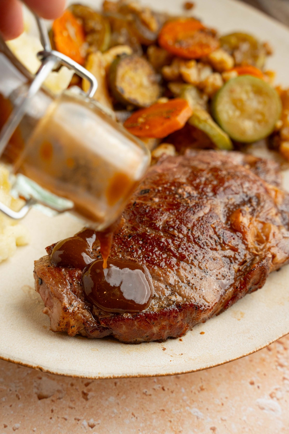 A condiment jar of A1 steak sauce pouring sauce on a steak. The steak is on a white plate with roasted vegetables.